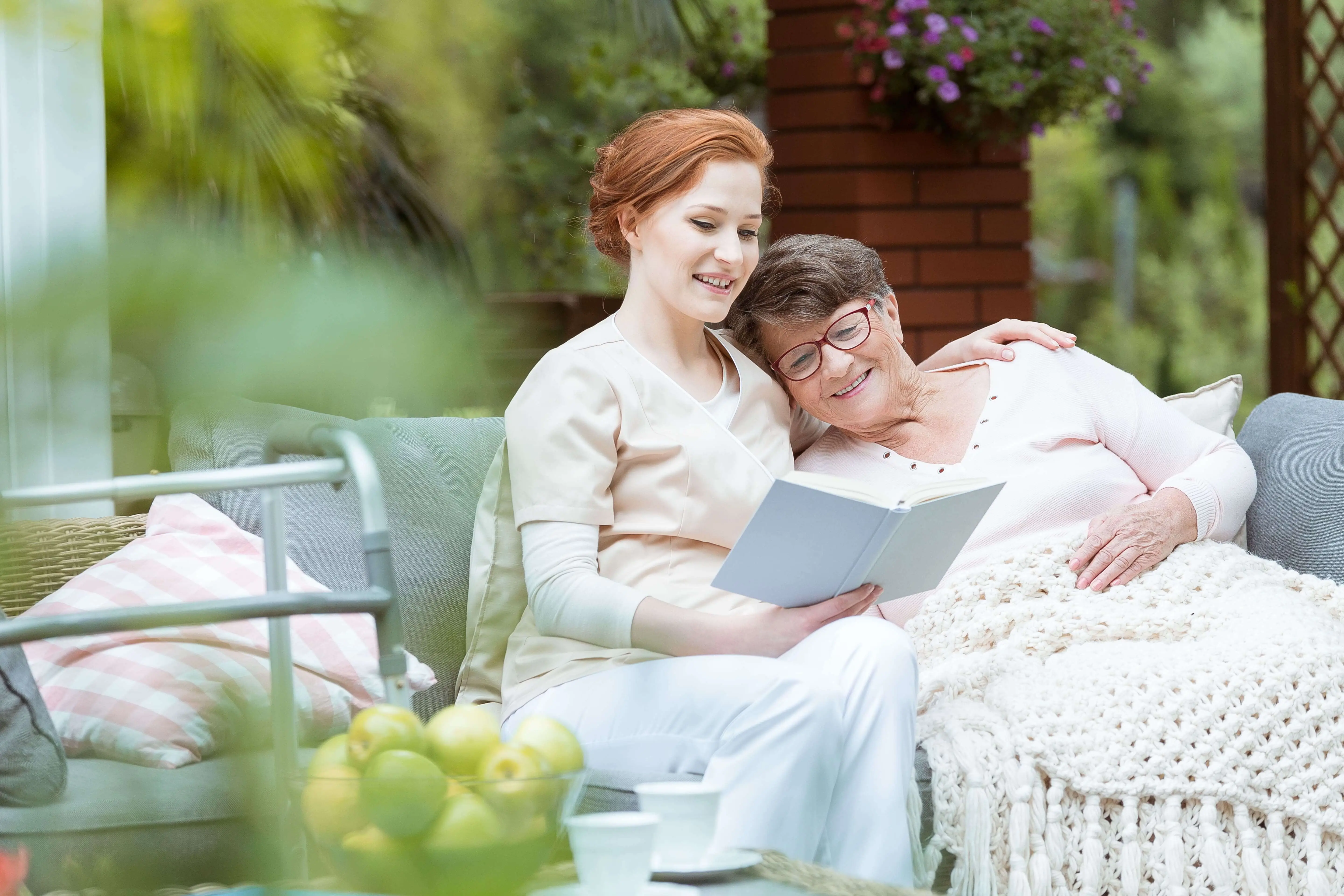 OC HomeCare caregiver offering compassionate senior care while reading with a smiling elderly woman in a serene outdoor setting in Orange County, California