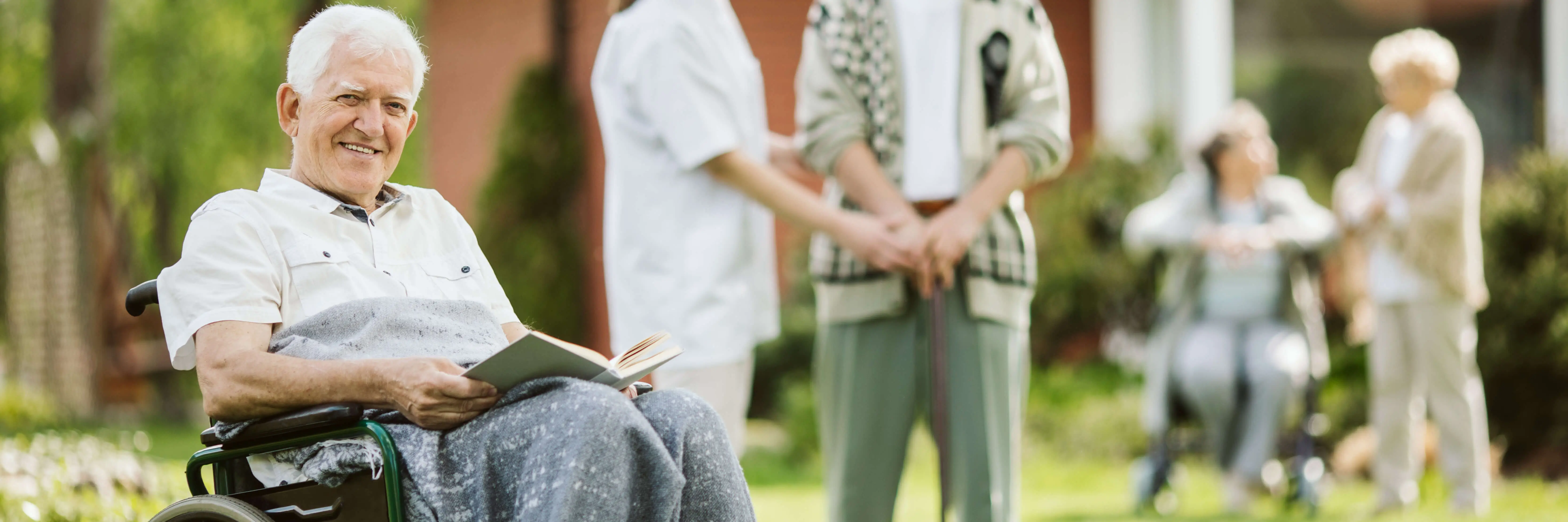 Elderly man smiling in wheelchair while reading outdoors at a licensed OC HomeCare residential care facility in Orange County, California