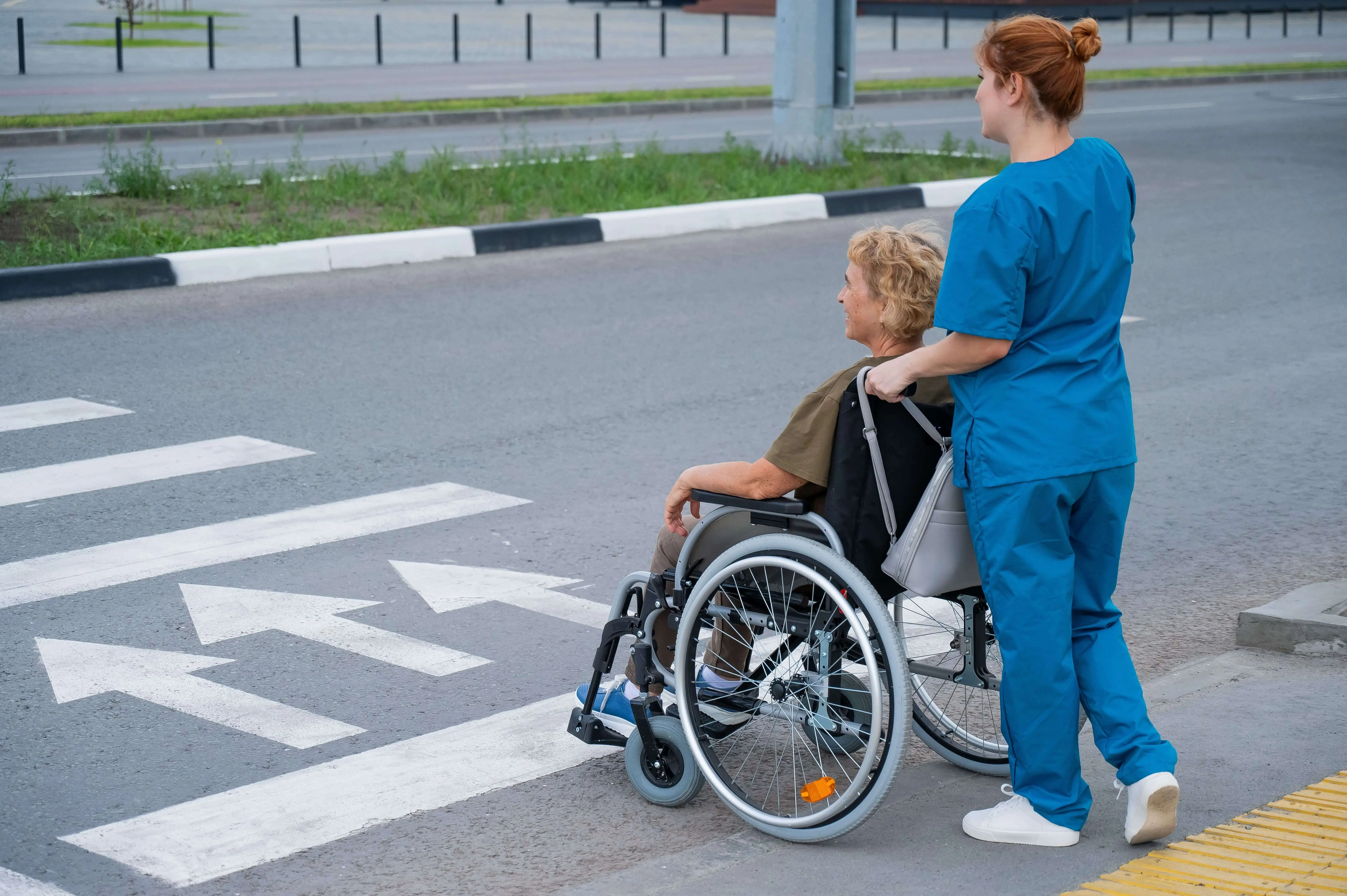 OC HomeCare caregiver assisting senior woman in wheelchair across crosswalk during non-emergency medical transportation in San Juan Capistrano, Orange County, CA